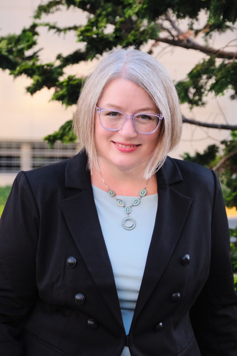 S. R. Mikulic smiling outdoors, wearing glasses and a dark jacket